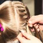 Hairdresser female hands makes braids for kid at barber shop, closeup